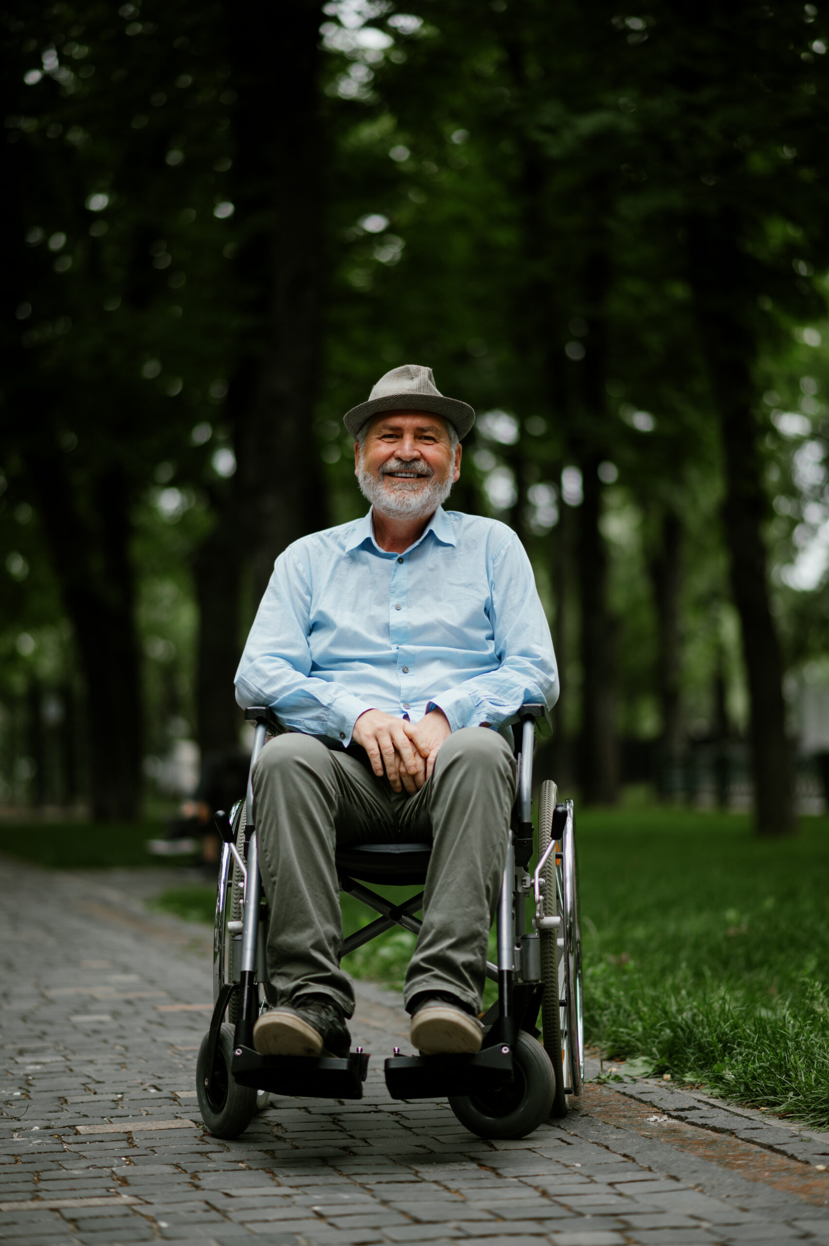 Elderly man in a wheelchair smiling in a park, symbolizing NDIS support for individuals with physical limitations.