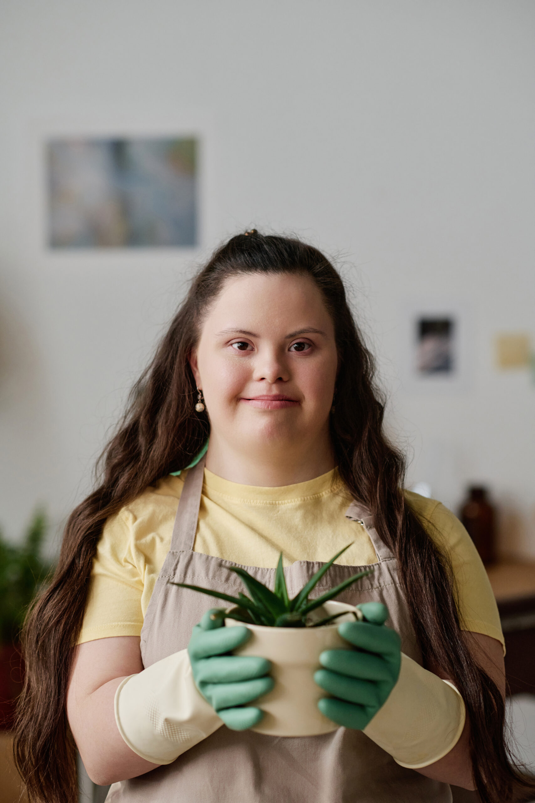 Young woman with Down syndrome smiling and holding a potted plant, representing NDIS household support services.