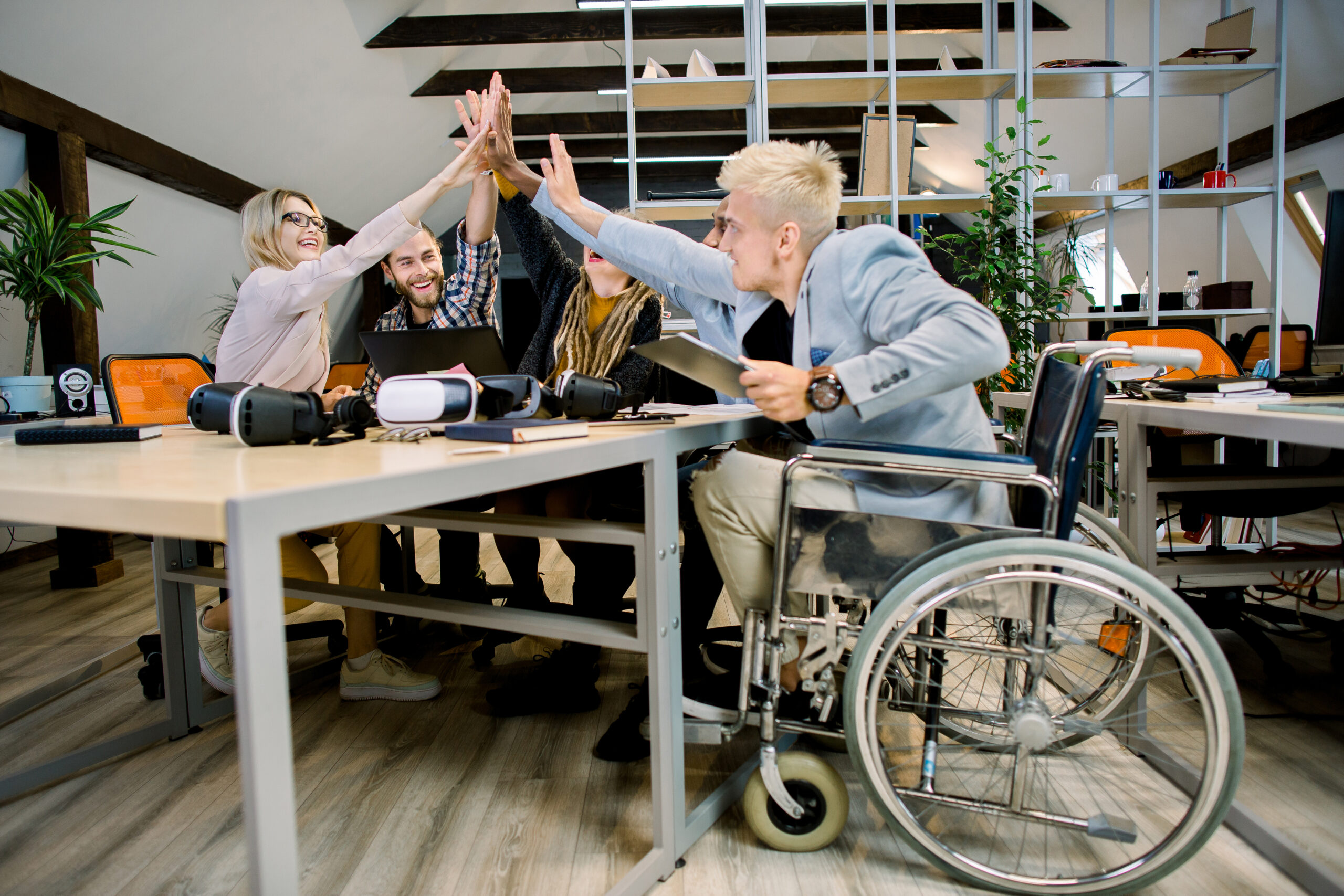 "Team of diverse coworkers, including a person in a wheelchair, high-fiving in a modern office setting"