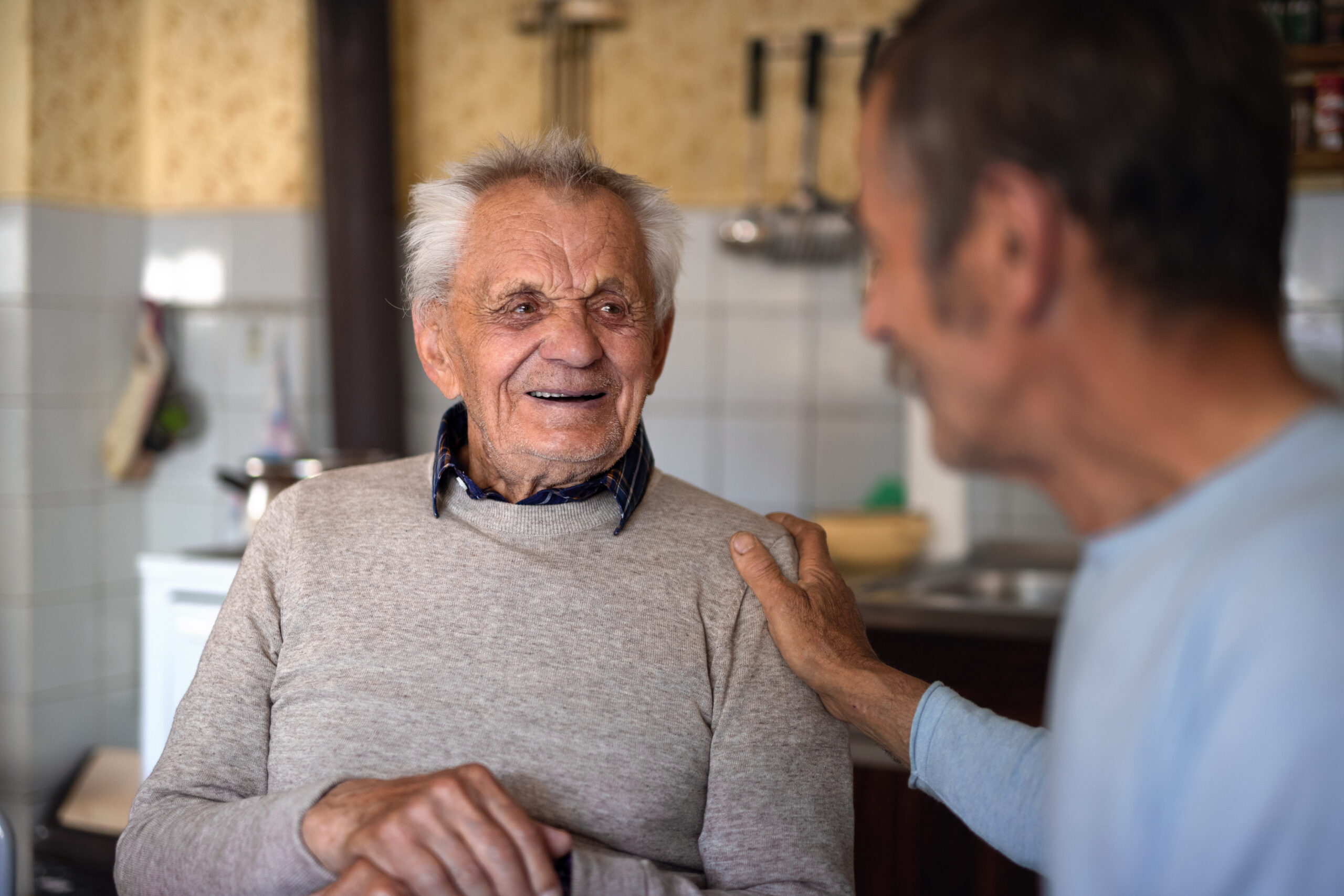 Elderly man smiling while talking to carer in kitchen – cost and FAQs about complex bowel care in NT under NDIS