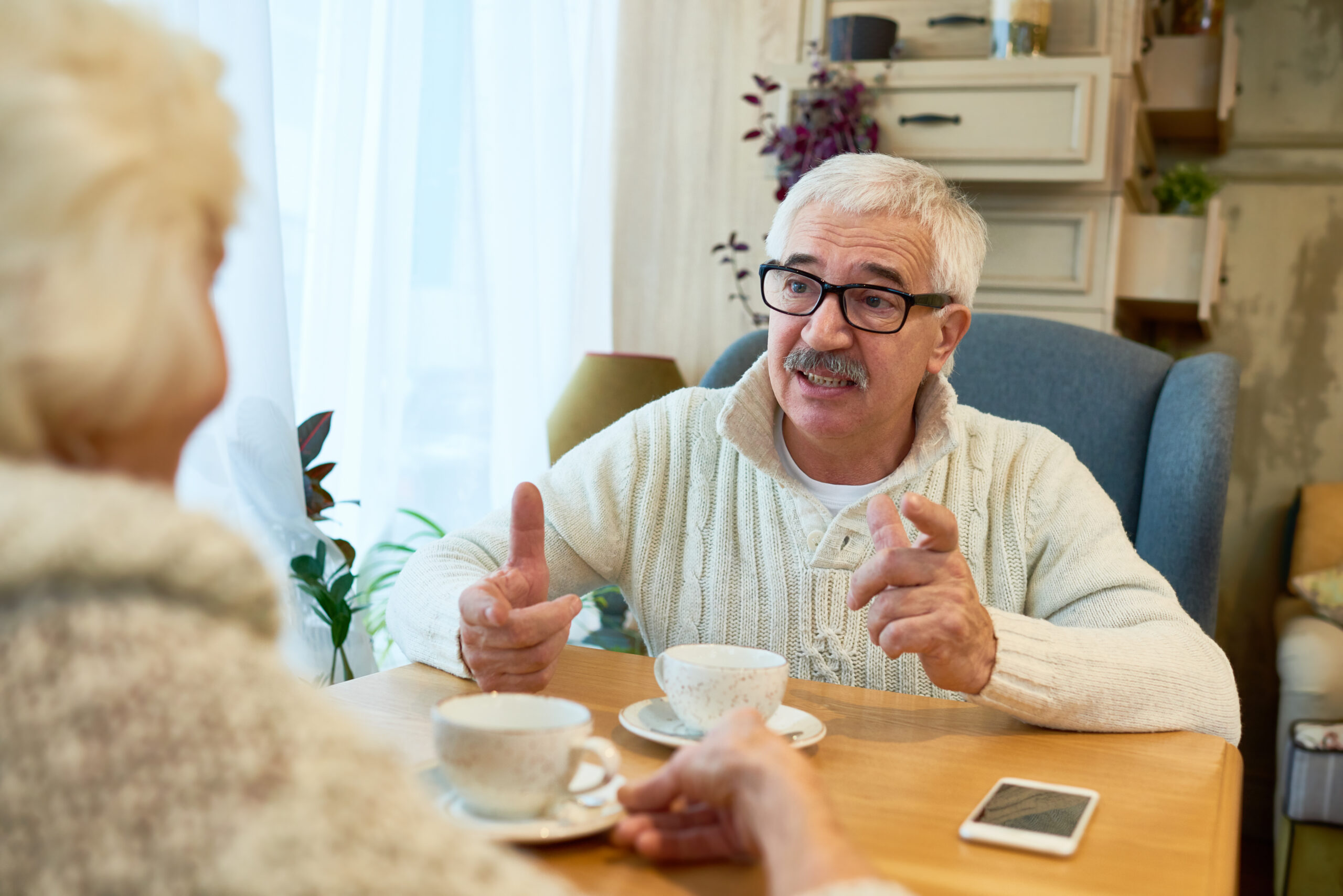 Elderly NDIS participant having a warm conversation with a support worker over tea, receiving assistance with social and community participation.