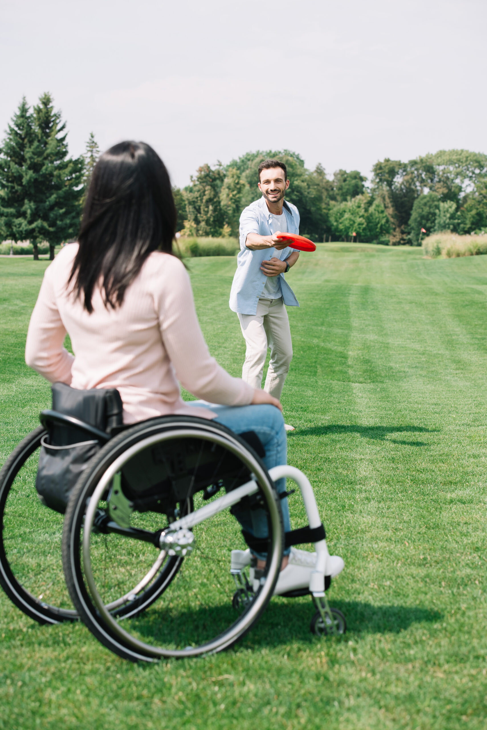Woman in a wheelchair playing frisbee outdoors with a support worker, showing NDIS daily tasks and shared independent living support.