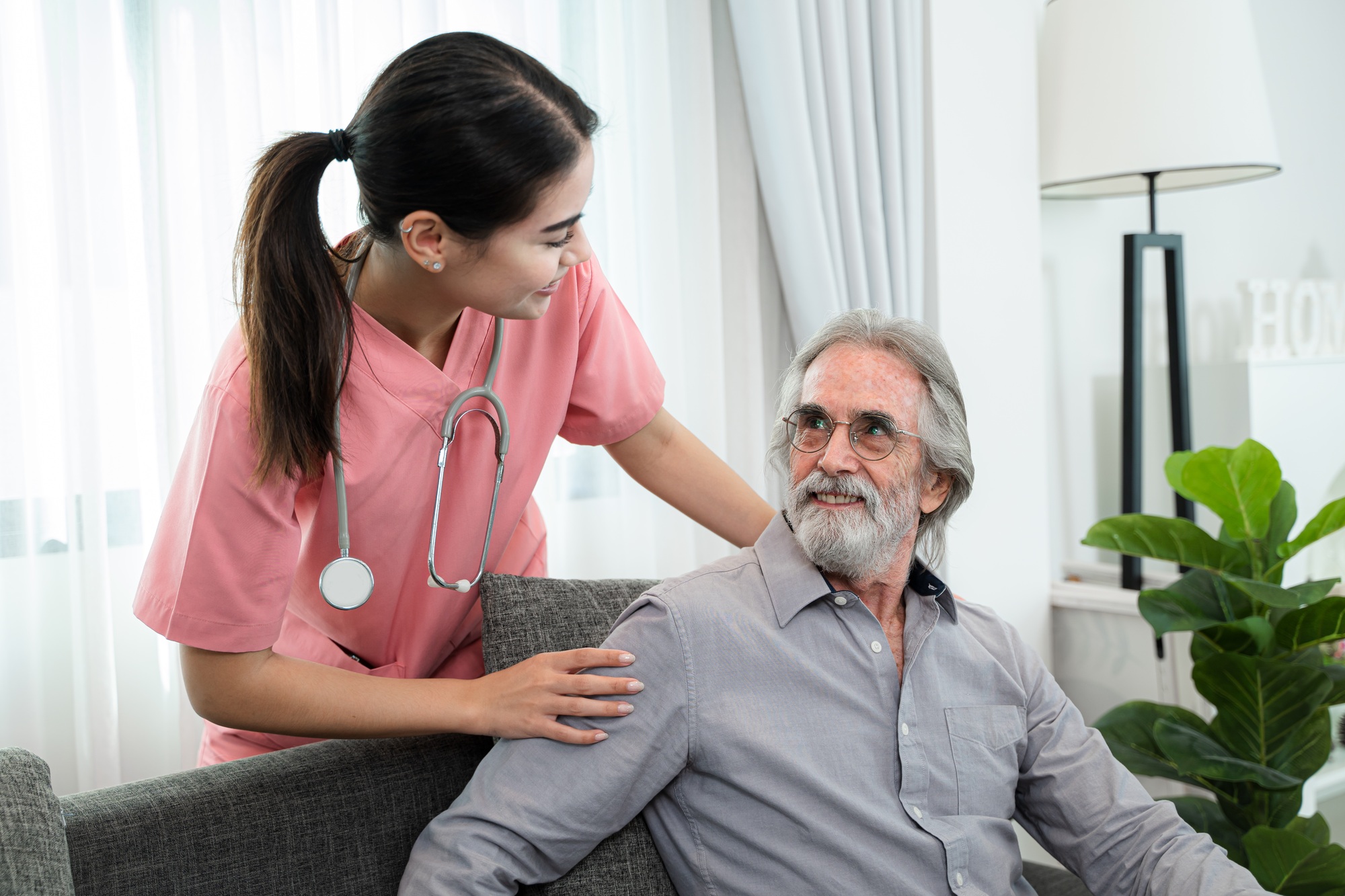 Young nurse smiling and supporting an elderly man during a home visit, symbolising compassionate community nursing care.