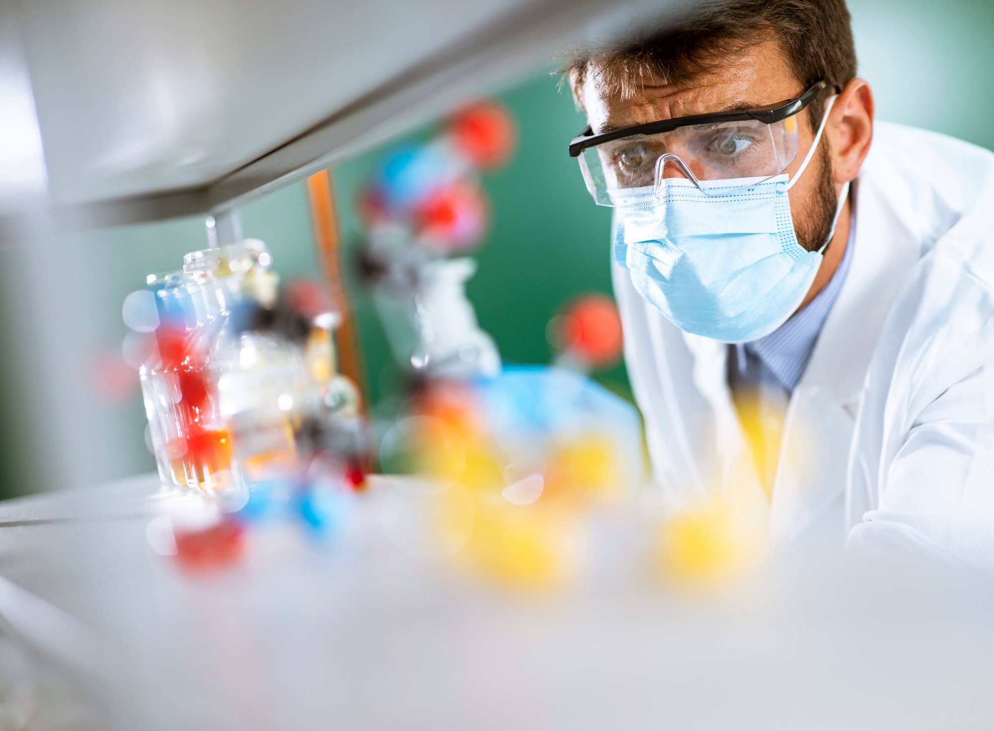 Young researcher with protective goggles checking test tubes